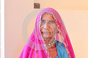 An indian elderly woman sitting in a pinkish red veil